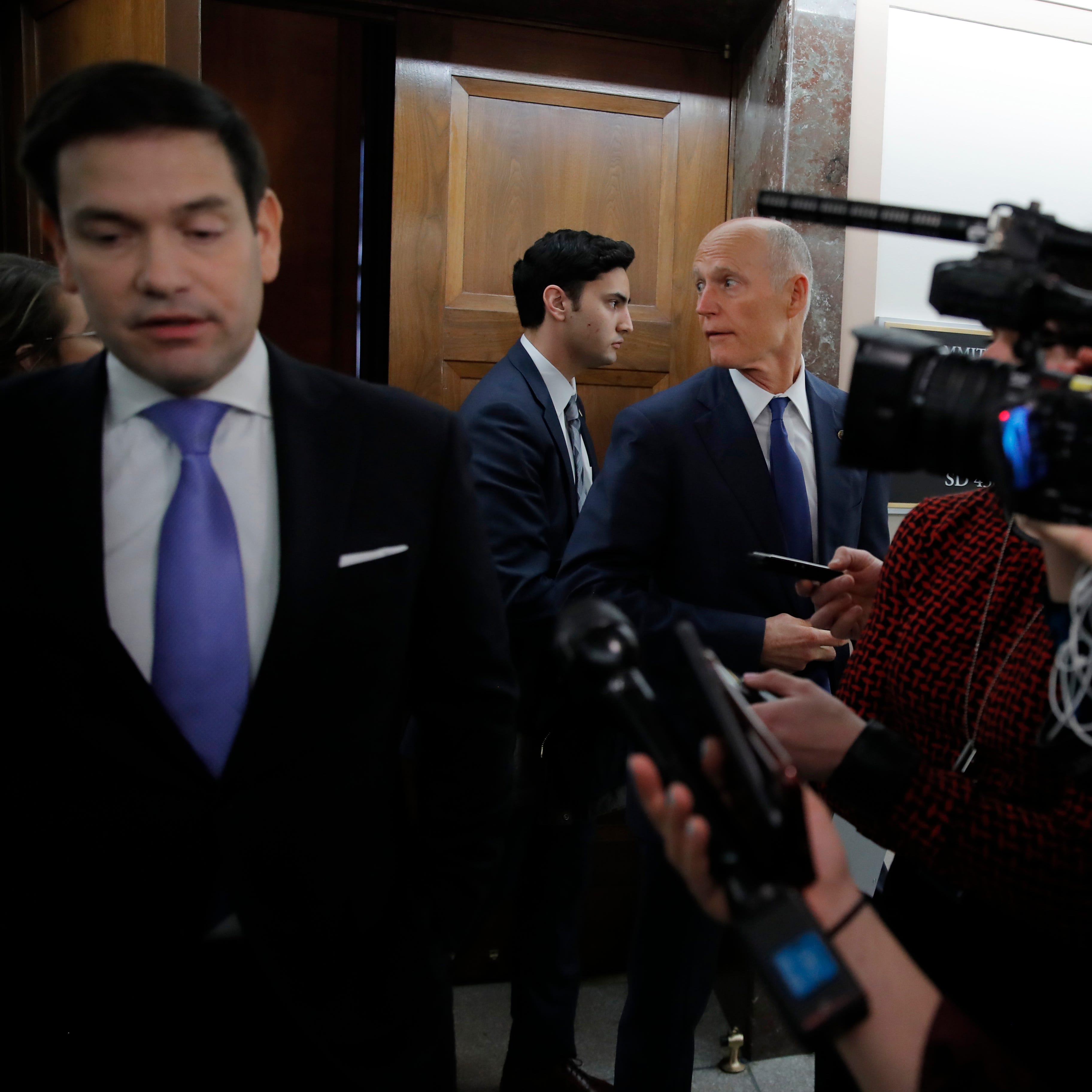 Sen. Rick Scott, R-Fla., center, looks back as he leaves a briefing on Capitol Hill in Washington, Thursday, March, 12, 2020, on the coronavirus outbreak, as Sen. Marco Rubio, R-Fla., speaks to the media at left.