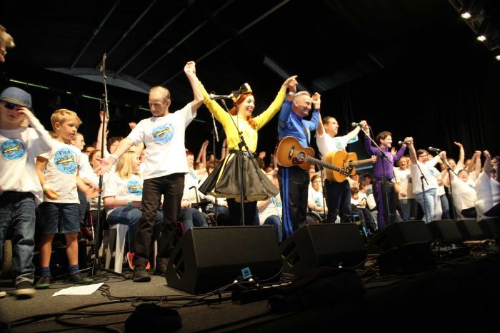 A large group of people hold hands on stage, preparing to take a bow.