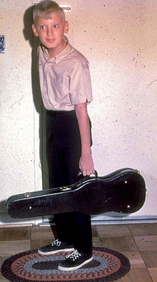 Young Glenn Gass stands near a closed door holding a violin case