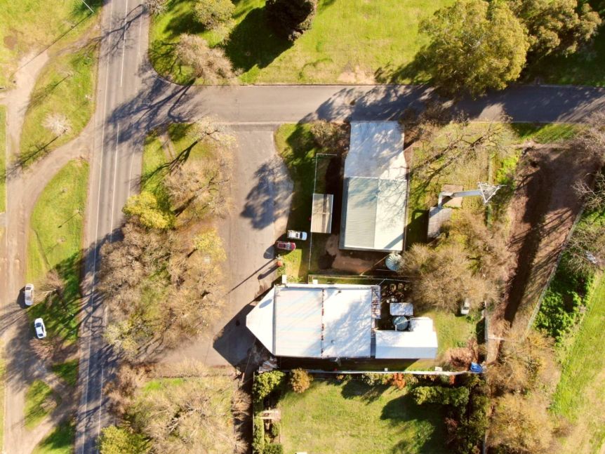 An aerial shot show a white-roof building surrounded by grass area and an unsealed road out the front.