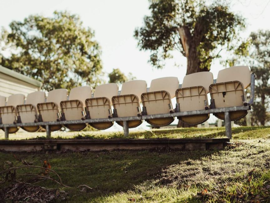 A row of empty plastic beige seats on grass at Mount Burr Football Club.