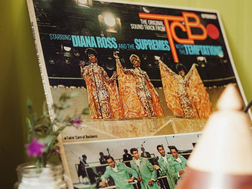 An old record sits on a shelf against a green wall. The record is the soundtrack from TCB starring Diana Ross and The Supremes.